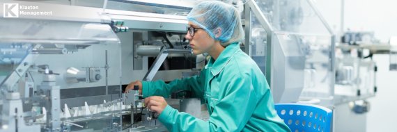 Profissional com jaleco, touca e óculos de proteção operando equipamentos em uma linha de produção de dispositivos médicos, ilustrando o rigor e os controles exigidos pela certificação ISO 13485.